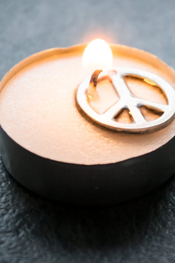 Close-up of a candle with a peace symbol, glowing warmly in the dark.